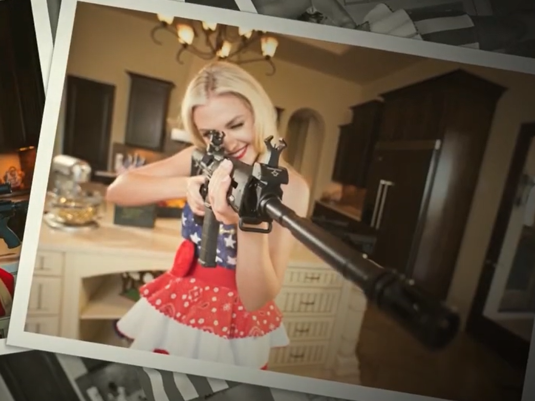 photo of Erika Frantzve from a gun manufacturing promo video. she is wearing a red, white, & blue star-spangled western outfit and has a rifle raised, looking down the sight.